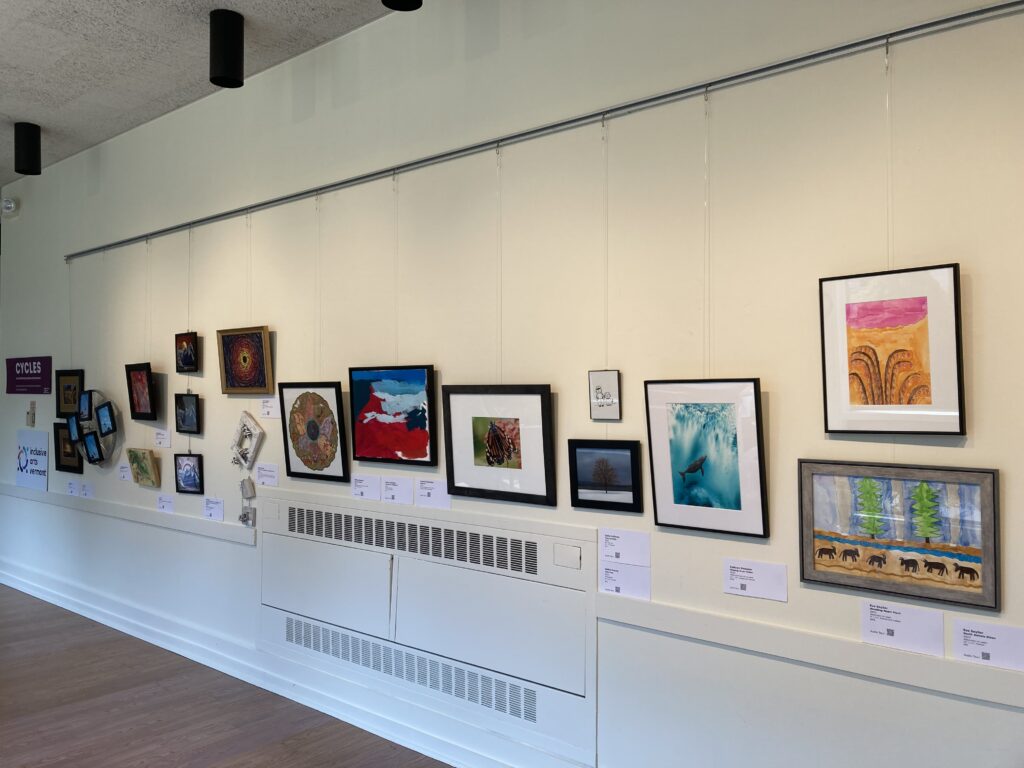 The CYCLES exhibition at the All Souls UU. The art is displayed on gallery walls. There are many pieces that are bright and colorful. 